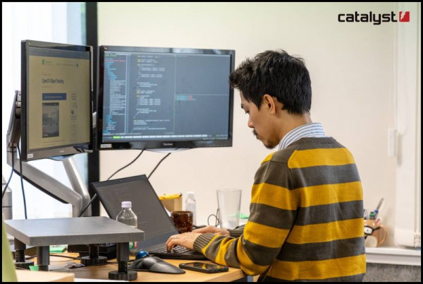 Looking over a person's shoulder at coding on a few computer screens.