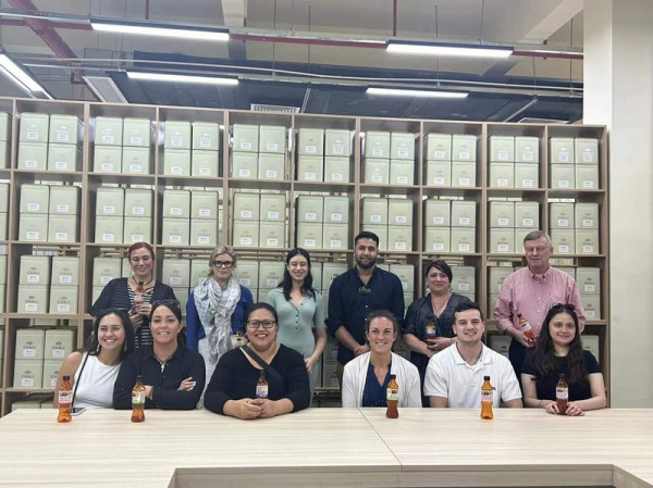 A group of people are sitting and standing in front of a row of boxes at the Chali tea factory.