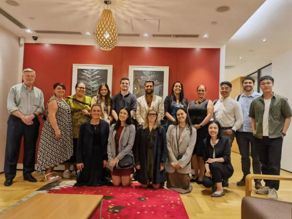 A group of people standing and sitting in front of a red wall with art on it at the NZTE office in Guangzhou.