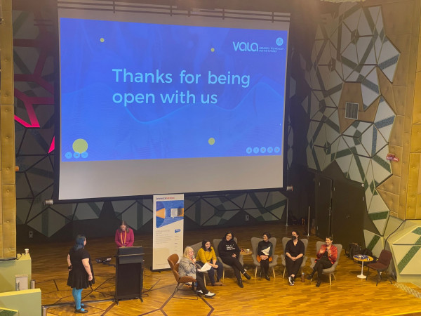 Picture of a presentation at the VALA conference. Speakers are seated on the stage underneath a presenation that says 'Thanks for being open with us'