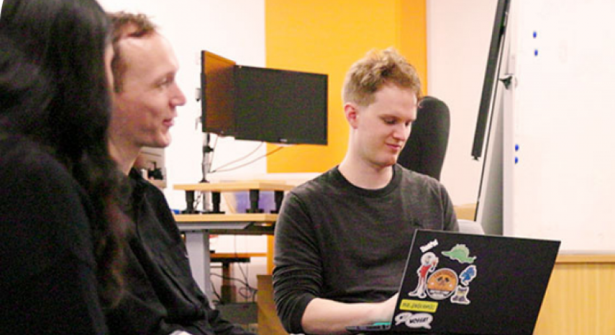 A man working on a laptop next to a man and woman in conversation