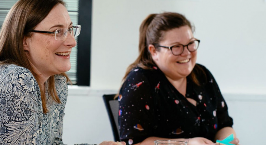 Two ladies from the Moodle team sit at a table smiling