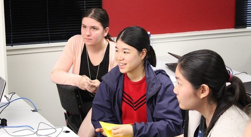 Three students are looking off camera towards a computer screen or instructor